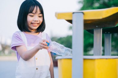 Asyalı küçük bir kızın resmi kullanılmış plastik şişeleri çöpe atıyor.