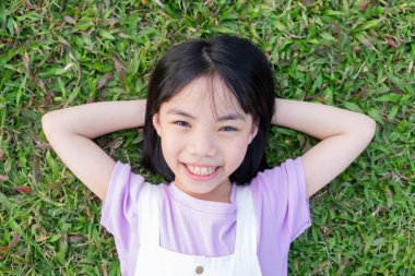 Parktaki çimlerin üzerinde yatan Asyalı küçük bir kız resmi