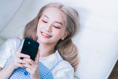 Genç Asyalı kız evde akıllı telefon kullanıyor.