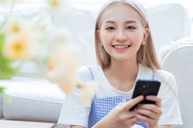 Genç Asyalı kız evde akıllı telefon kullanıyor.