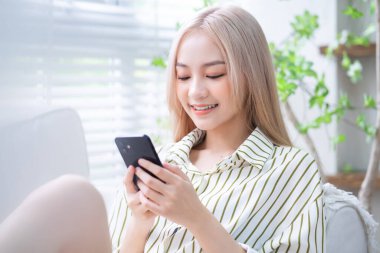 Genç Asyalı kız evde akıllı telefon kullanıyor.