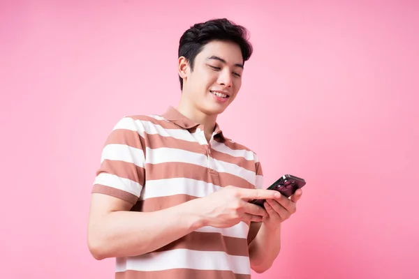ピンクを背景にスマートフォンを使ったアジア系青年の肖像 — ストック写真