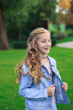 Pozitif mavi gözlü, sarı saçlı, kot ceketli, güneşli bir günde yeşil çimenlikte bir kız.