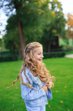 Pozitif mavi gözlü, sarı saçlı, kot ceketli, güneşli bir günde yeşil çimenlikte bir kız.