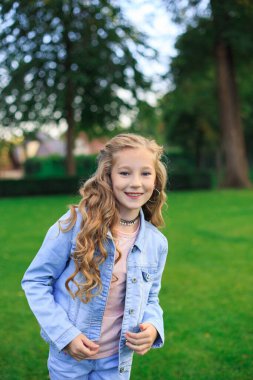 Pozitif mavi gözlü, sarı saçlı, kot ceketli, güneşli bir günde yeşil çimenlikte bir kız.