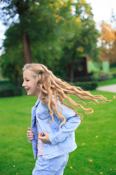 Pozitif mavi gözlü, sarı saçlı, kot ceketli, güneşli bir günde yeşil çimenlikte bir kız.