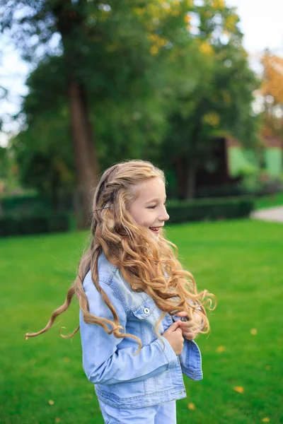 Pozitif mavi gözlü, sarı saçlı, kot ceketli, güneşli bir günde yeşil çimenlikte bir kız.