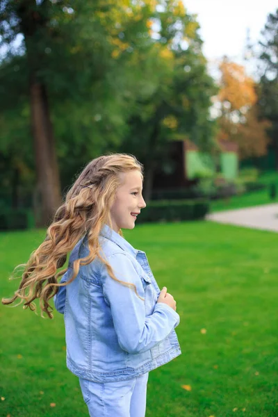 Pozitif mavi gözlü, sarı saçlı, kot ceketli, güneşli bir günde yeşil çimenlikte bir kız.