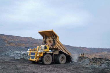 Büyük sarı bir çöp kamyonu mineralleri boşaltıyor. Madencilik ve minerallerin taşınması süreci. Açık çukur yöntemiyle maden çıkarma.