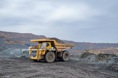 Büyük sarı bir çöp kamyonu mineralleri boşaltıyor. Madencilik ve minerallerin taşınması süreci. Açık çukur yöntemiyle maden çıkarma.