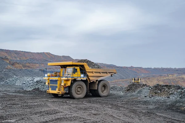 Büyük sarı bir çöp kamyonu mineralleri boşaltıyor. Madencilik ve minerallerin taşınması süreci. Açık çukur yöntemiyle maden çıkarma.