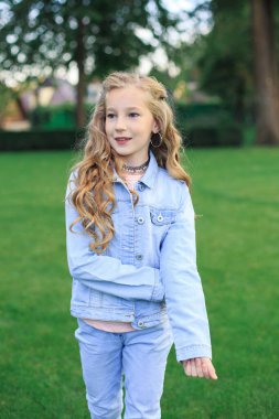 Neşeli sarı saçlı, mavi gözlü bir kızın portresi, yeşil çimlere karşı mavi kot ceketli bir kız.