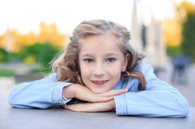 Masada oturan neşeli, sarı saçlı, mavi gözlü bir kızın portresi. 