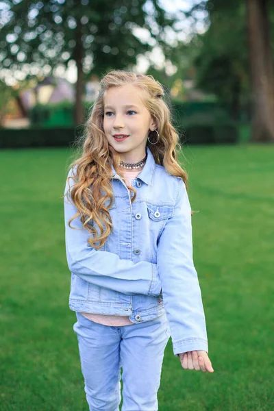 Neşeli sarı saçlı, mavi gözlü bir kızın portresi, yeşil çimlere karşı mavi kot ceketli bir kız.