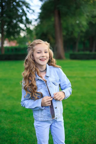 Neşeli sarı saçlı, mavi gözlü bir kızın portresi, yeşil çimlere karşı mavi kot ceketli bir kız.