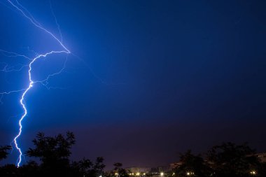 Bulutlar ve gök gürültüsü, fırtına rüzgarları, gece şehrin üzerindeki şimşekler.