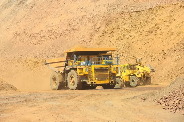 A quarry dump truck loaded with orange rock. Moving large dump trucks around the quarry.  Open-pit mining technology.
