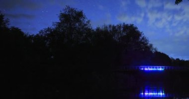 Yıldızların gece gökyüzünde, renkli arka ışıklandırma ve gece manzarasının zamanlaması ile birlikte hareket etmesi. Ağaçların silueti.