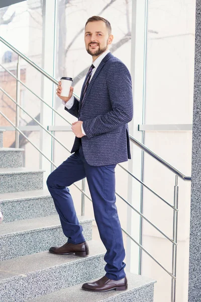 A young man in a business suit on the stairs with a glass of coffee. A businessman on the stairs.