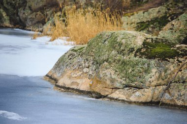 Taşlı nehir kıyısında, kışın kızıl granit nehir kıyısında. Donmuş bir nehir ya da kayalık bir göl.