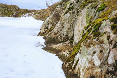 Taşlı nehir kıyısında, kışın kızıl granit nehir kıyısında. Donmuş bir nehir ya da kayalık bir göl.