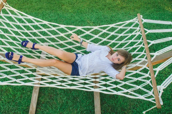 A young woman is resting in a white hammock. Portrait of a girl in a hammock in cloudy weather.