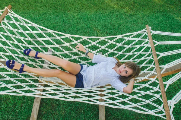 A young woman is resting in a white hammock. Portrait of a girl in a hammock in cloudy weather.
