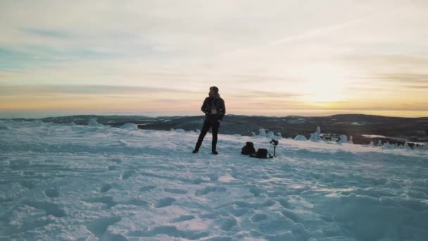 El hombre está parado en una montaña al atardecer en un paisaje invernal — Vídeo de stock