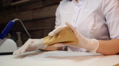 Tıbbi koruyucu beyaz eldivenli profesyonel manikürcü steril manikür aletleriyle bir kese kağıdı açar. Manikür güzellik salonunda müşteri hizmetlerine hazırlanılıyor.
