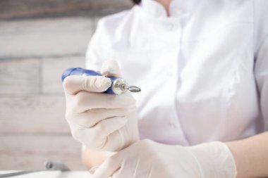 Tıbbi koruyucu beyaz eldiven giyen profesyonel bir manikürcü manikür salonundaki manikür matkabını açıyor..