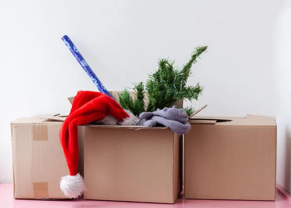 Üç karton kutu, birinde yapay Noel ağacı Noel Baba şapkası ve ambalaj kağıdı var..