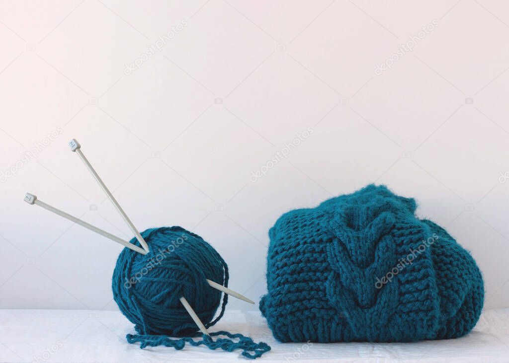 Large knitting needles are stuck into a large ball of blue yarn next to a product knitted from yarn.