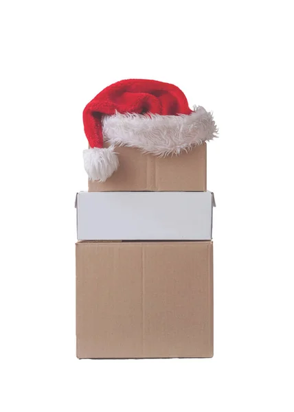 Three cardboard boxes stand on top of each other on top of Santa Clauss red hat isolated image — Stock Photo, Image