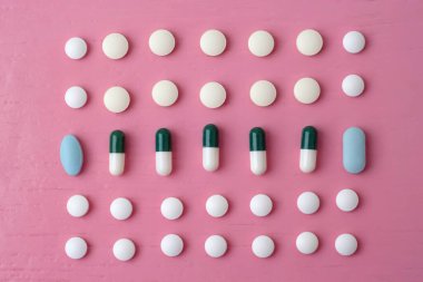 Parlak pembe arka planda, farklı boyutlarda tabletler, renkler ve şekiller satırlara dizilir