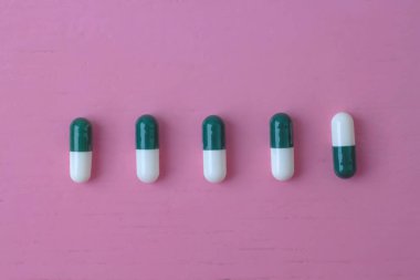 Parlak pembe arka planda biri baş aşağı olmak üzere beş tane iki renkli hap var.