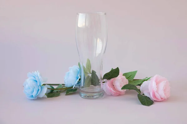 Pembe ve mavi çiçekler pembe arka planda şeffaf bir bira kadehinin yanında. — Stok fotoğraf