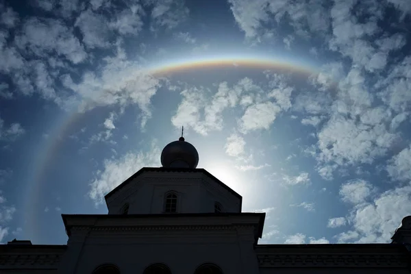 Rainbow halo in the blue sky with white clouds. Magical natural rainbow effect with the sun. Temple silhouette against the beautiful sky