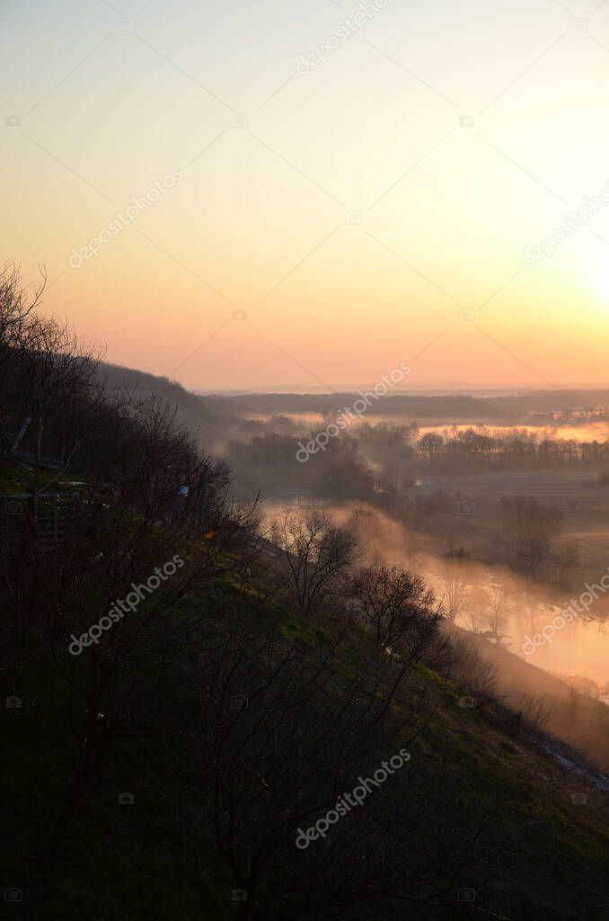 Picturesque sunrise over a foggy meadow and river on a summer morning. Vertical photo. World Environment Day concept.