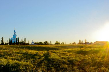 Valaam adasındaki yeşil bir arazide batan güneşin ışınları. Uzaktaki Şekil Değiştirme Katedrali.