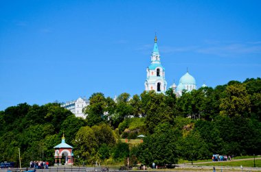 Spaso-Preobrazhensky Valaam Manastırı. Ormanın yeşilinde mavi gökyüzüne karşı güzel bir katedral. Dağın eteklerinde turist grupları.