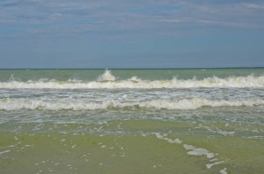 Yaz bulutlu bir günde deniz manzarası. Küçük dalgalar kumsalda yuvarlanıyor.