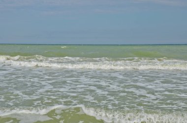 Küçük dalgalar kumlu bir sahilde yuvarlanıyor. Bulutlu bir yaz gününde deniz kıyısı manzarası.