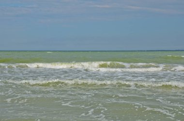 Küçük dalgalar kumlu bir sahilde yuvarlanıyor. Bulutlu bir yaz gününde deniz kıyısı manzarası.