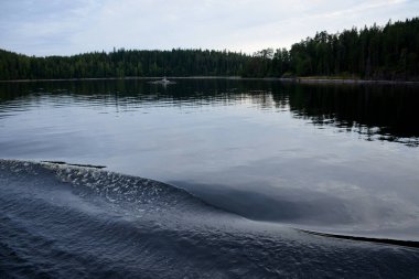 Gölün üzerinde gün batımı bulutlu gökyüzü, ormanlı adaların siluetleri. Kuzey doğanın sakin fotoğrafı.