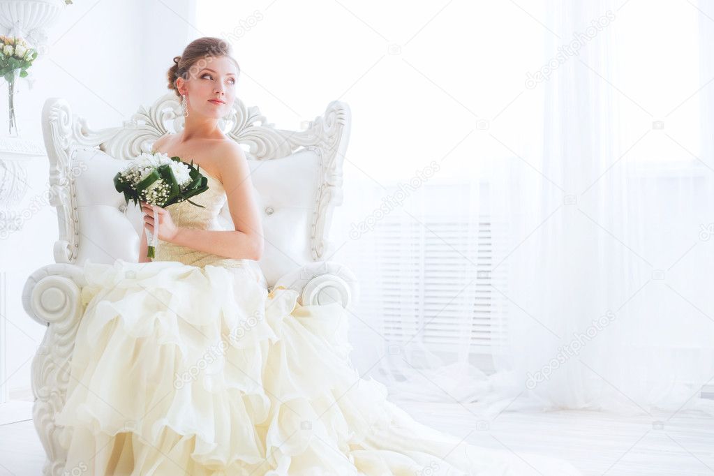 Young bride is sitting in an armchair with flowers.