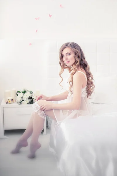 Beautiful girl lying on the white bed with flowers. — Stock Photo, Image