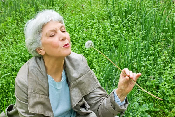 Mulher idosa feliz sentado em um prado na primavera grama verde e — Fotografia de Stock