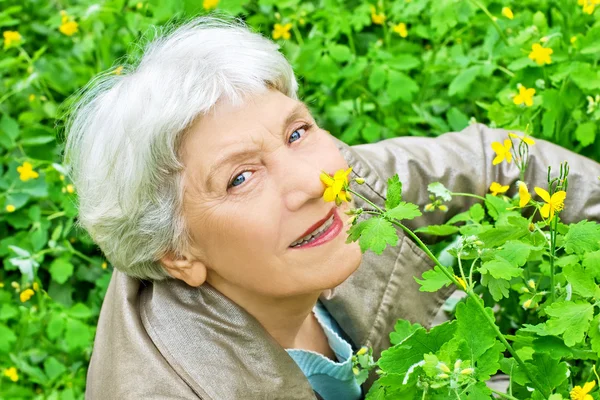 Happy elderly woman sitting on a glade of yellow flowers in spri