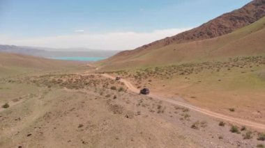 Two SUVs are driving among the mountains to a beautiful lake. Road on a dirt road. Beautiful view of the mountain lake from the top. Alpine lake Bartogay. Off-road adventure in the mountains
