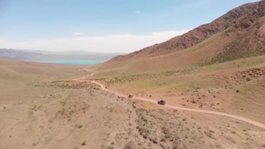 Two SUVs are driving among the mountains to a beautiful lake. Road on a dirt road. Beautiful view of the mountain lake from the top. Alpine lake Bartogay. Off-road adventure in the mountains